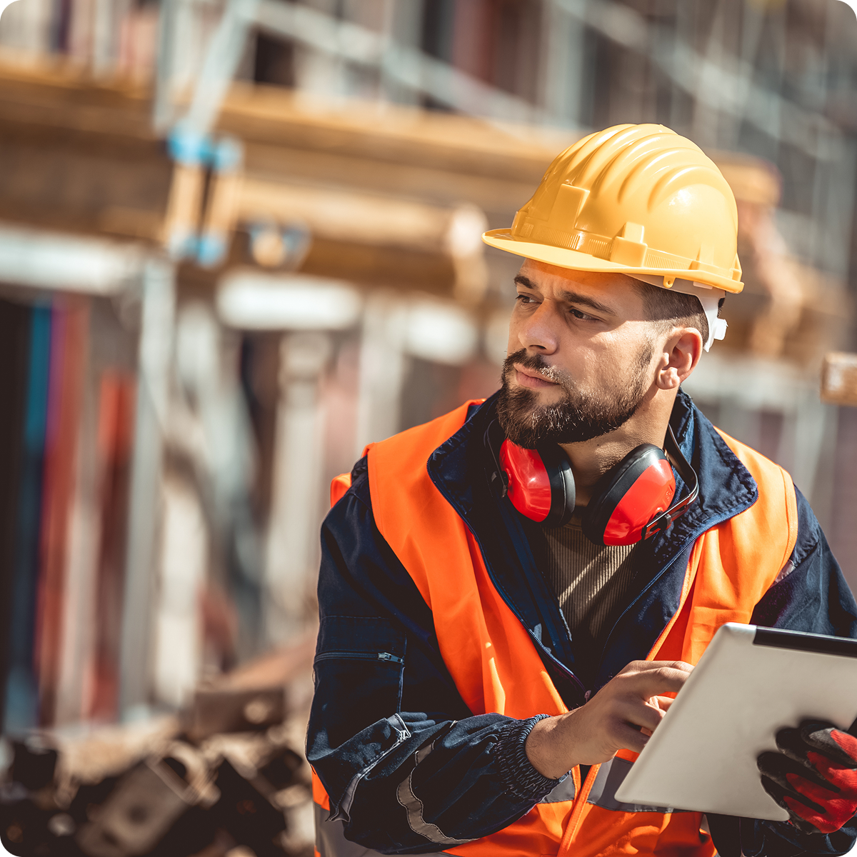 Construction worker in the field holding onto paper documents and looking at the project with a confused look on his face