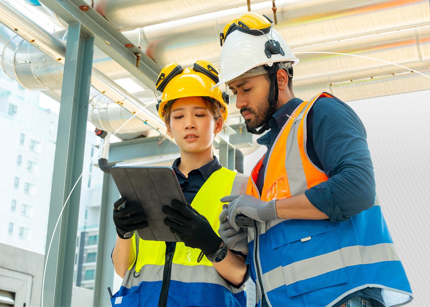 An MEP contractor wearing a hard hat and safety vest checks building system plans on a tablet at a construction site.