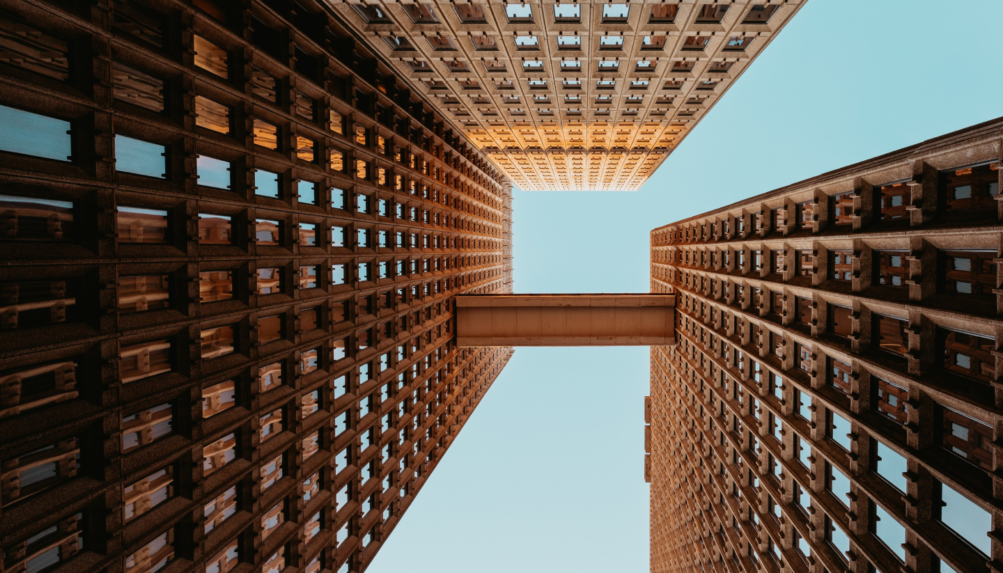 Upward view of two tall brick buildings connected by a skybridge against a clear blue sky.