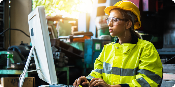 A construction worker in a jacket and hard hat works at a computer.