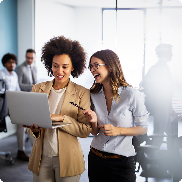 Two female office employees discuss over a laptop.
