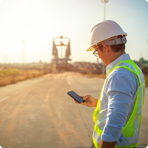 A man in a hard hat and vest looks down on a sunny construction site.