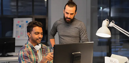 Image shows 2 men working at a computer and talking