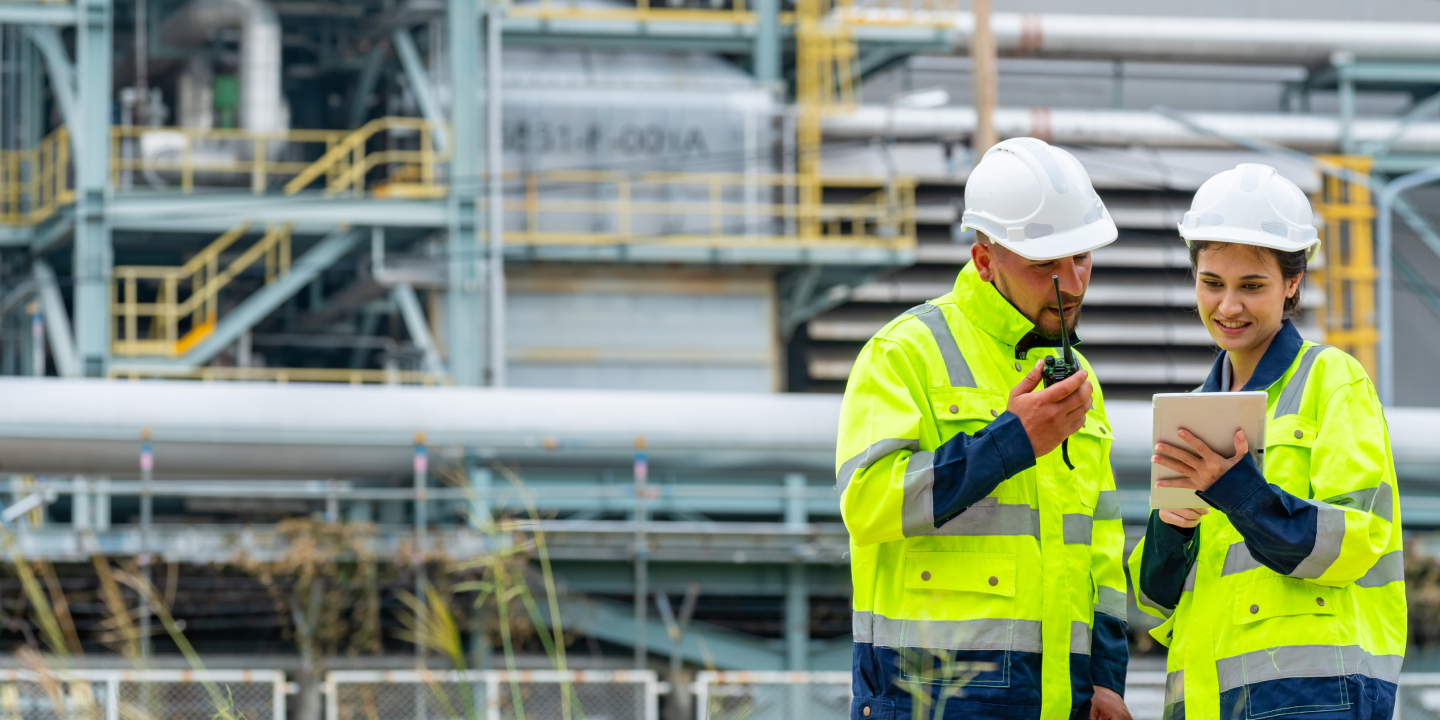 A man and woman in construction gear look at a tablet on site