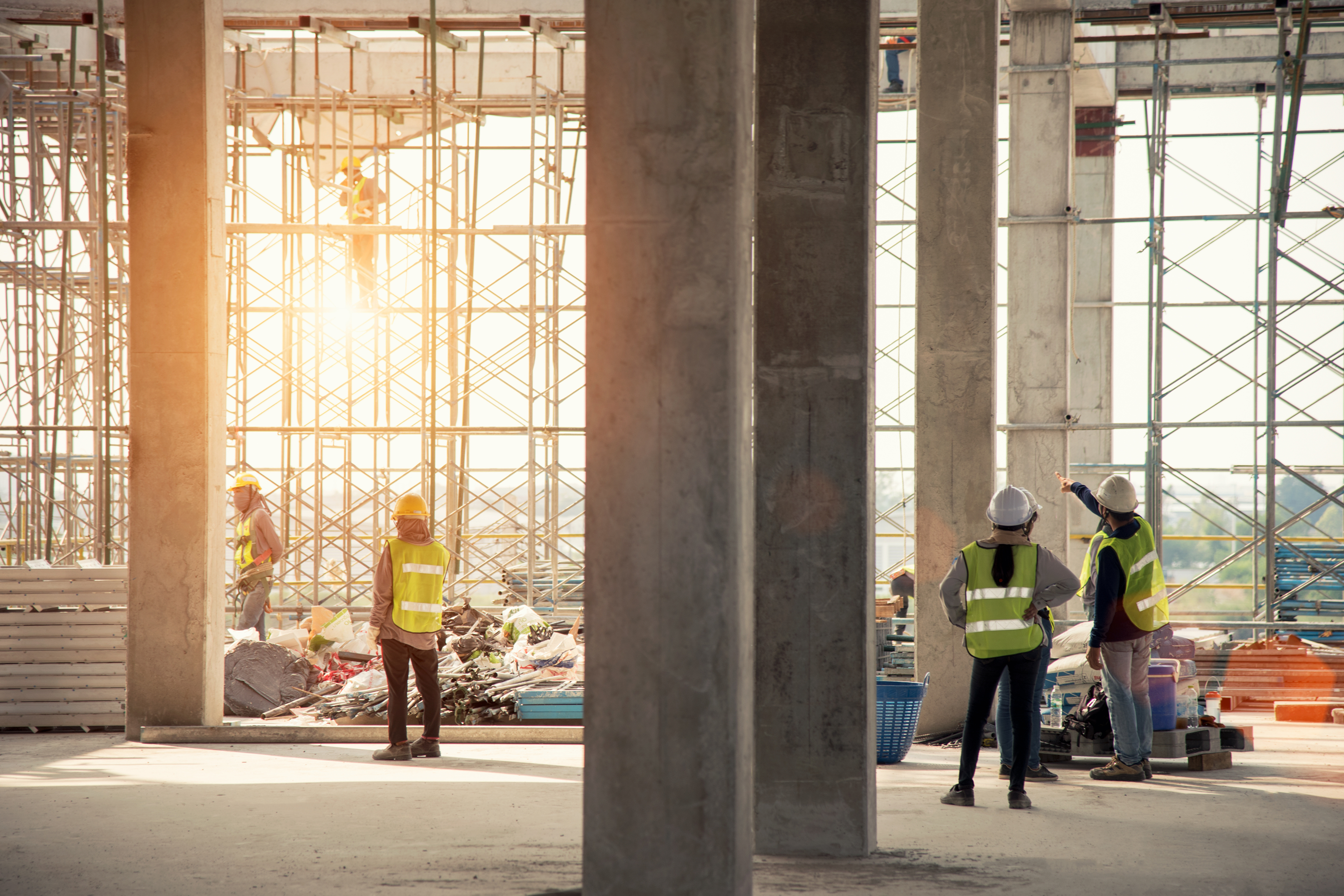 A man in a hard hat and vest talks with someone and points to the site while three others in safety gear continue working.