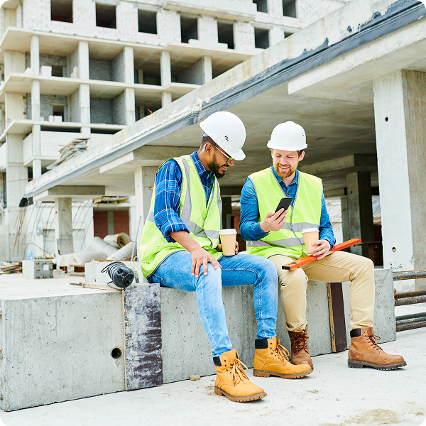 Two construction workers look at a phone on a project site.