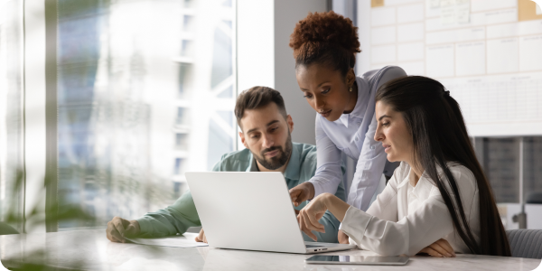 Three employees work around a computer in an office.