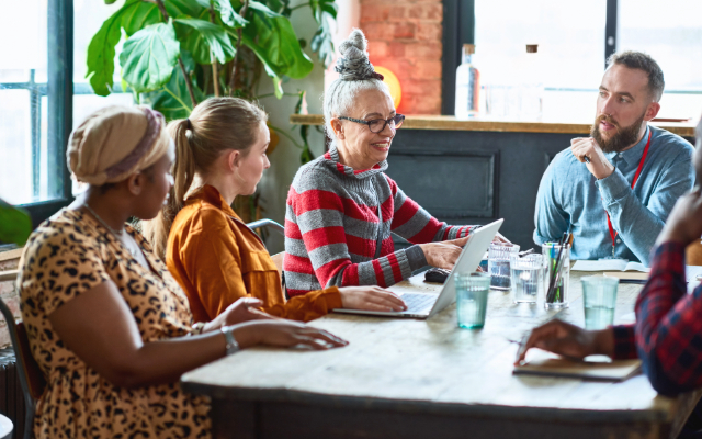 Diverse group of colleagues collaborating around a table with a laptop.