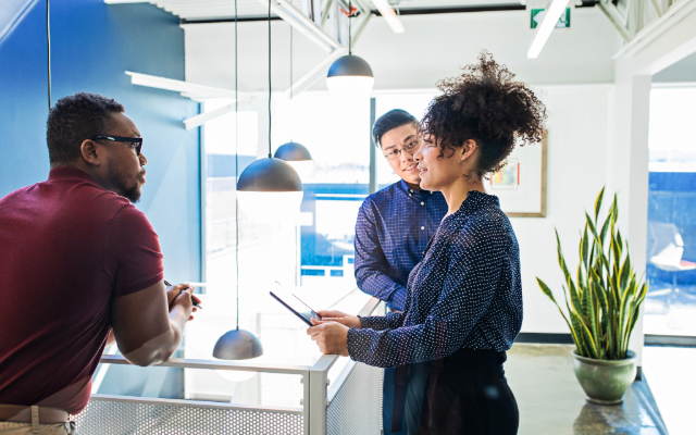 A group of three business professionals conversing casually in a bright office environment.