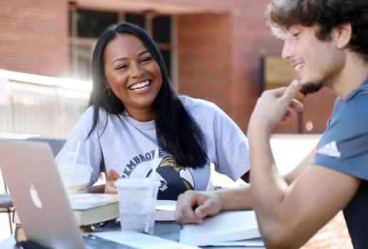 Students laughing and studying together at a table outside.