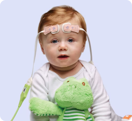 Baby wearing a ForeSight Jr and holding a green stuffed frog against a soft light-blue background.