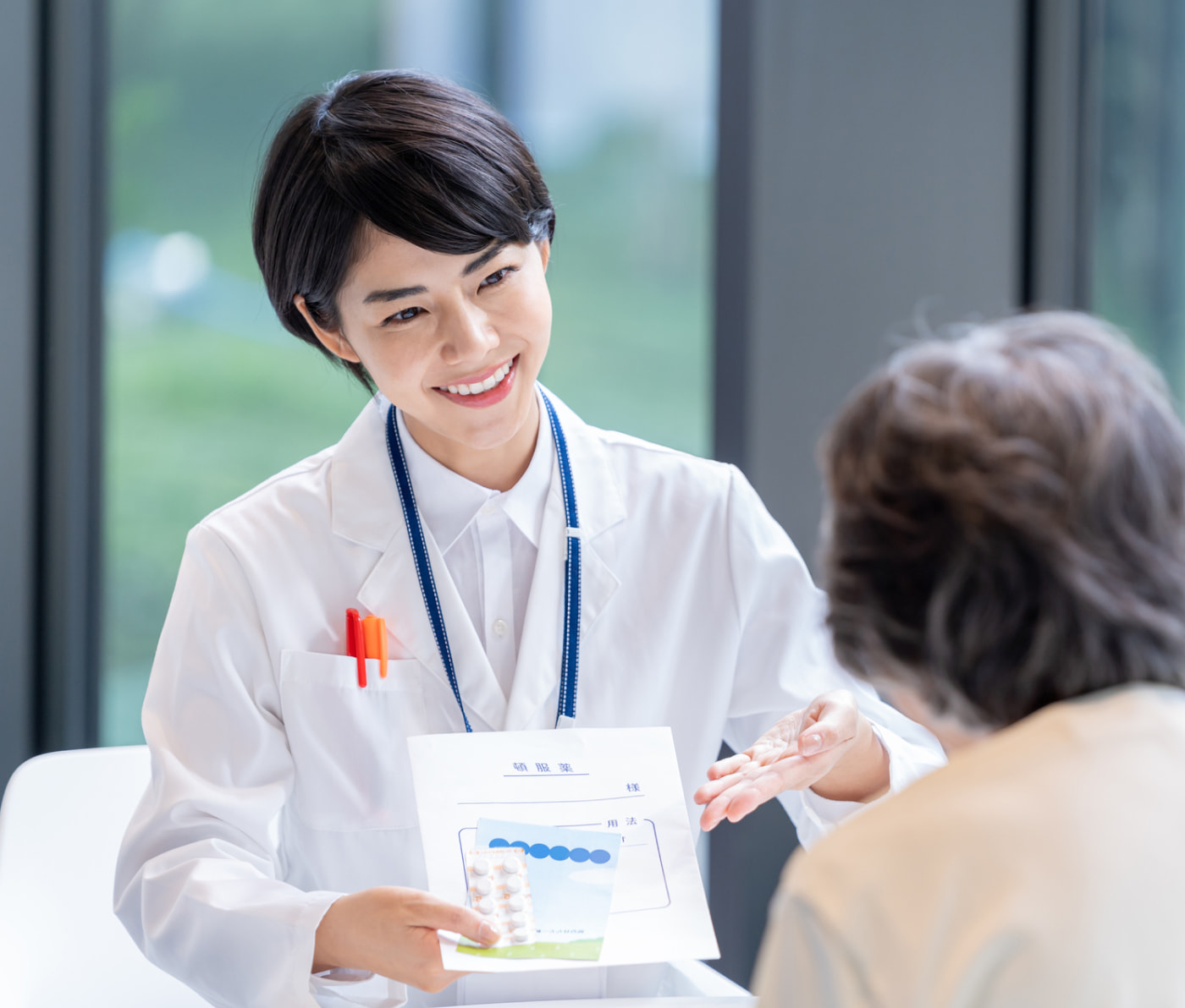 女性の薬剤師が患者に薬の説明をしている様子。