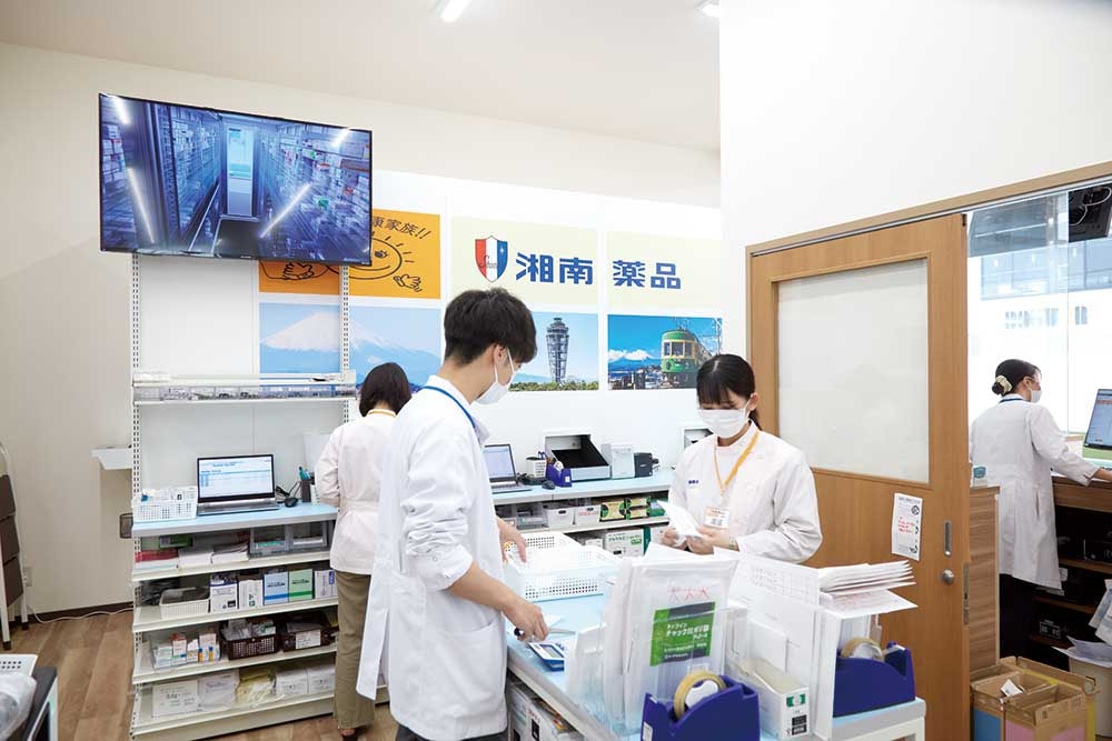 薬局内でマスクと白衣を着用した薬剤師が調剤作業をしている様子。