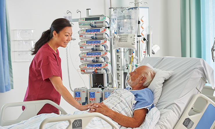 Female nurse standing bedside with mature male patient