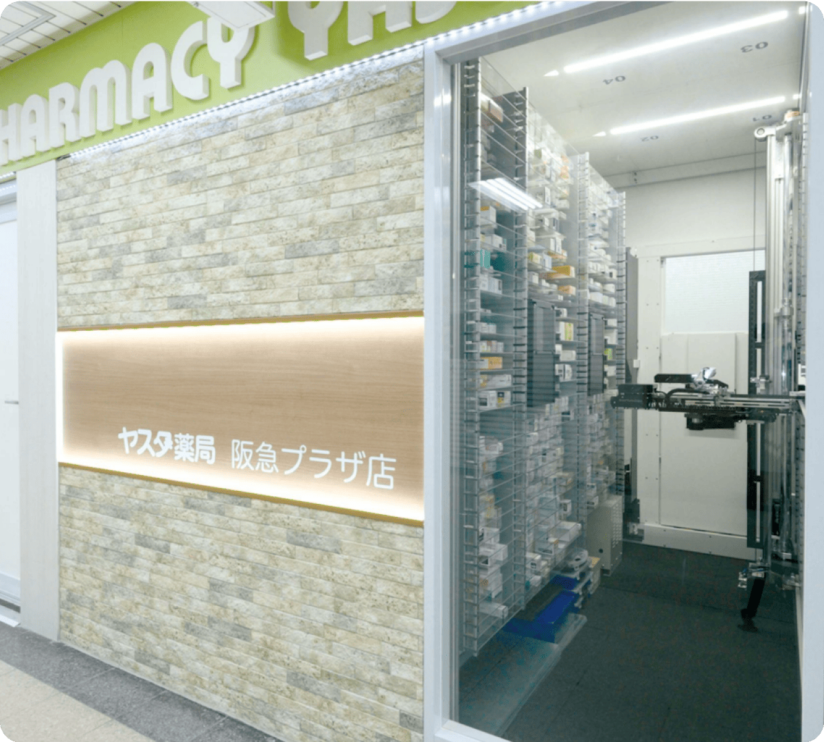 ヤスタ薬局阪急プラザ店の入口と、ガラス越しに見える薬剤自動分注システム。