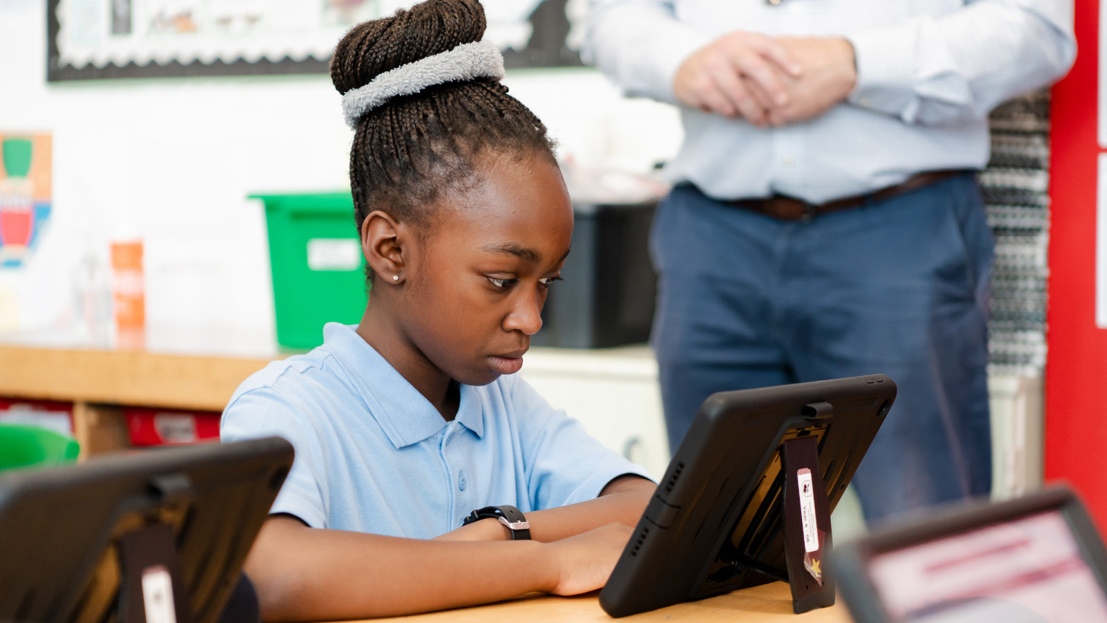A young student focused on a tablet in a classroom setting.