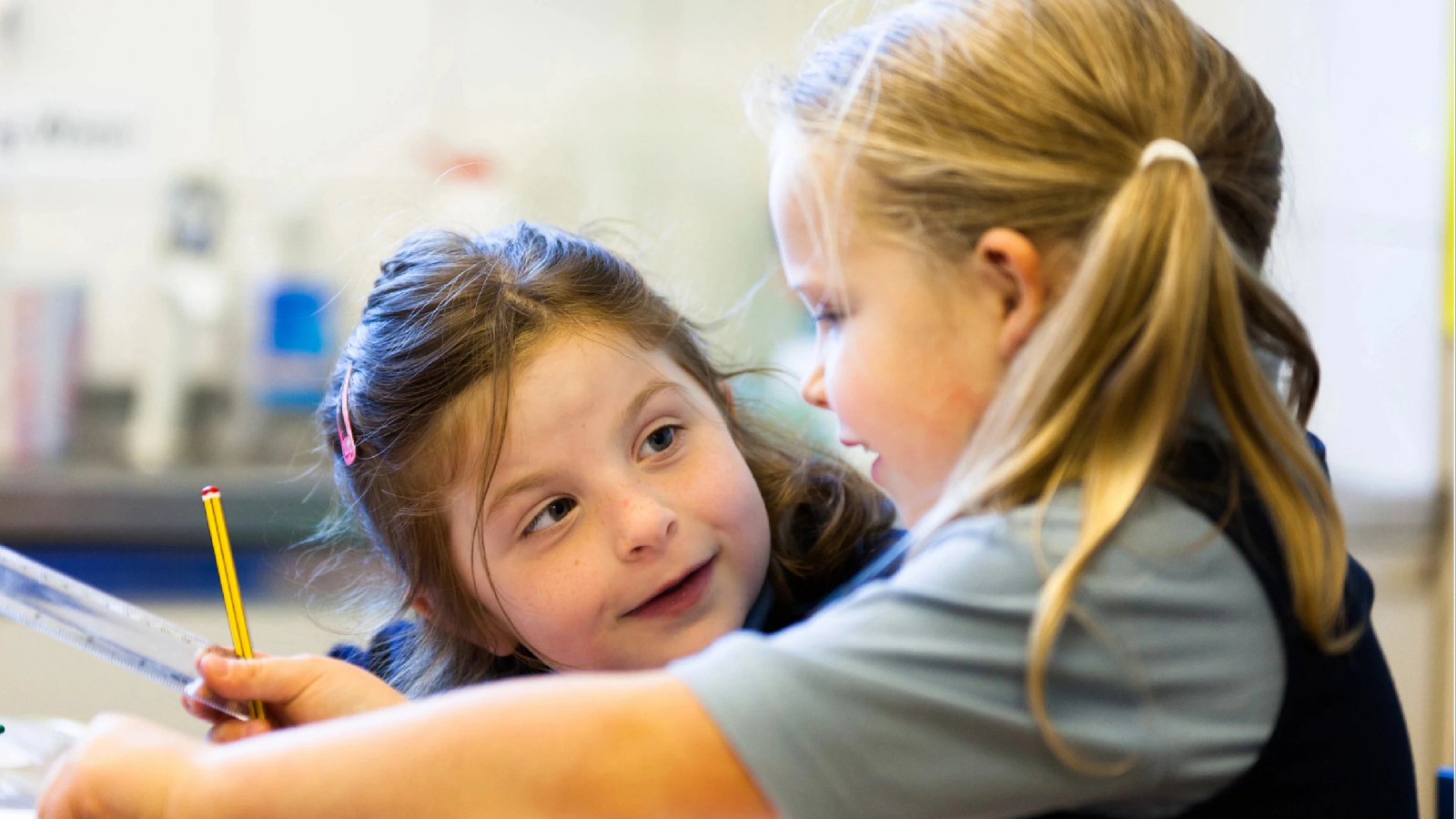 Close-up of two elementary school-aged girls looking at each other, engaged in learning.