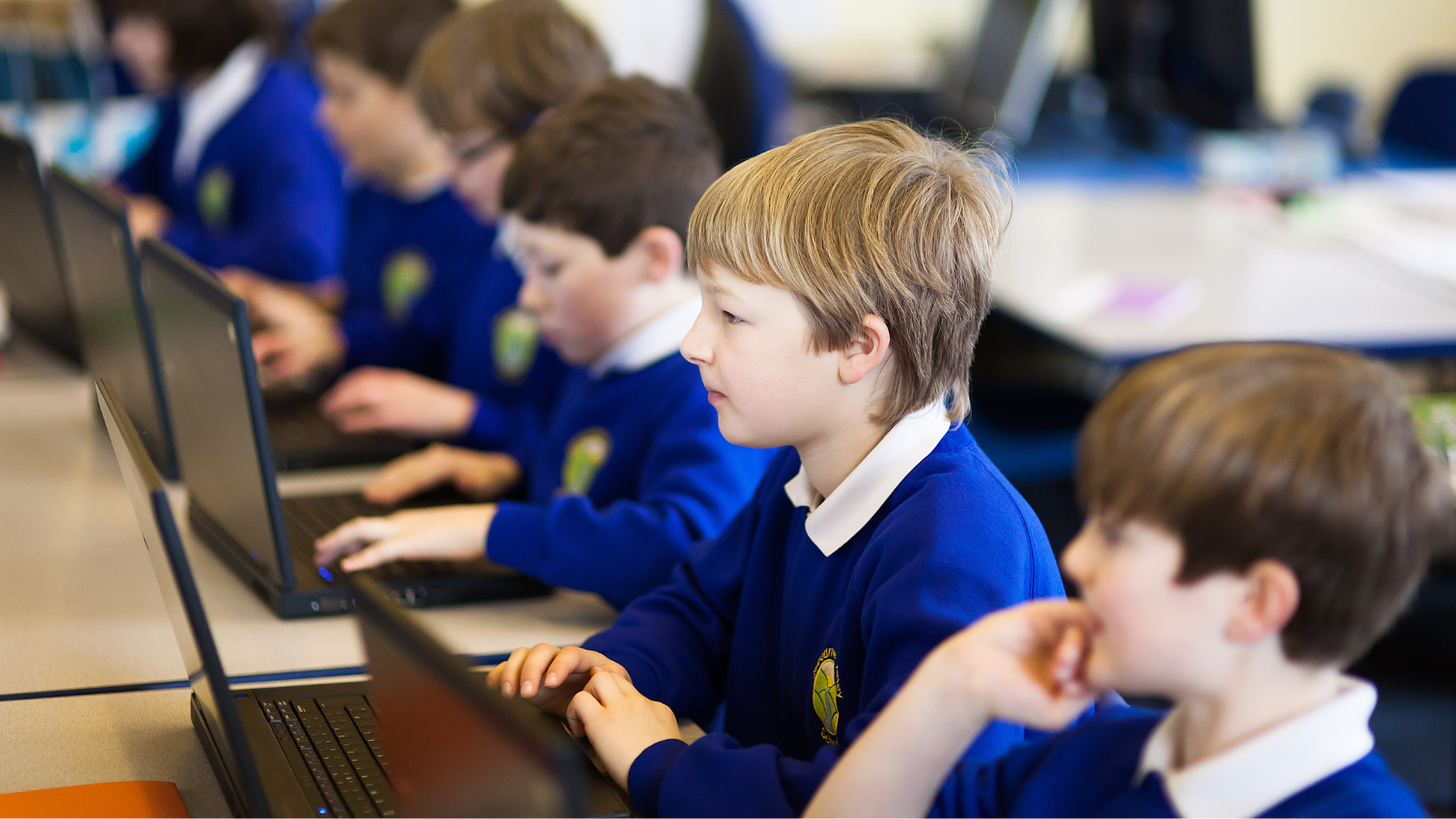 Young students in blue uniforms focused on laptops in a classroom setting.