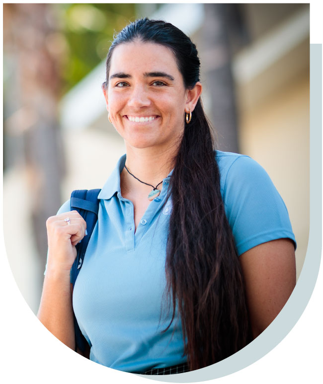 A smiling woman with long dark hair, on a University of St Augustine for Health Sciences campus with a backpack.