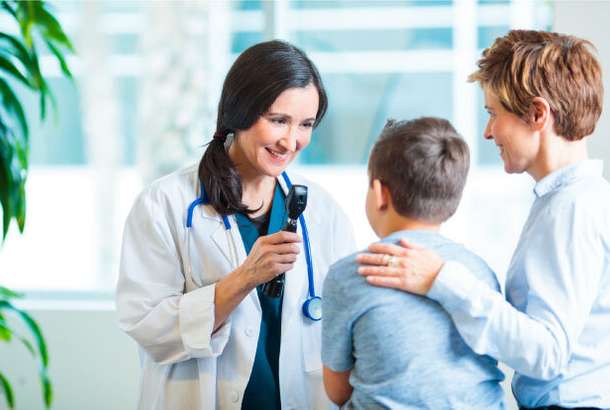 A pediatrician interacts kindly with a child during an examination, with the child's mother present.