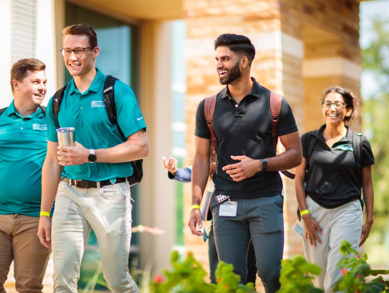 Happy students or colleagues walking on a sunny campus path with backpacks and casual attire.