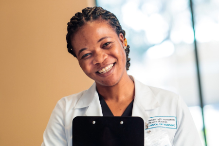 A friendly female medical professional wearing a lab coat and holding a black clipboard.