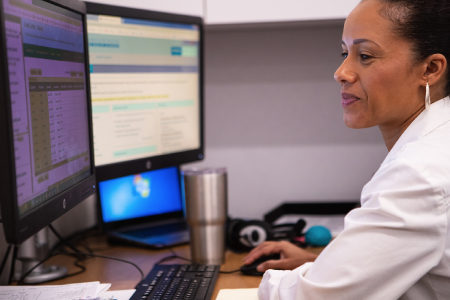 Professional woman focused on her work at a multi-monitor computer setup.