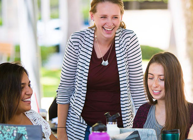 Three young women laughing and smiling, possibly at an outdoor gathering or study session.