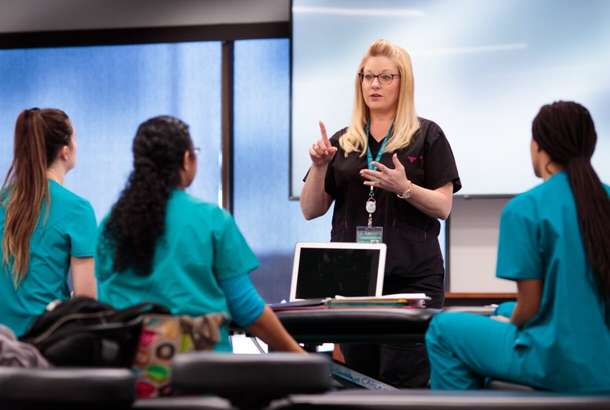 An instructor speaks to three students during a medical training session.