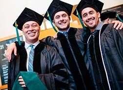 Three smiling graduates in caps and gowns, celebrating their achievement.
