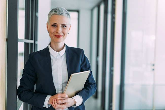 Confident businesswoman in a dark suit jacket holding a silver tablet.