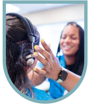 A person adjusting headphones on another person's head, both smiling.