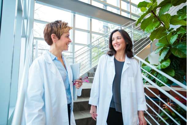 A doctor shares digital data with a person in a suit, while another medical professional is seated nearby.