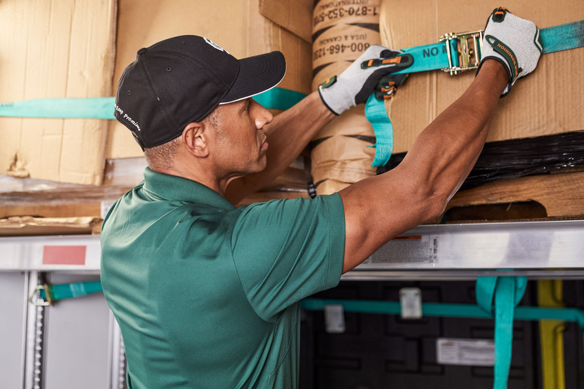 Close-up of a person in a uniform adjusting a cargo strap on boxes.