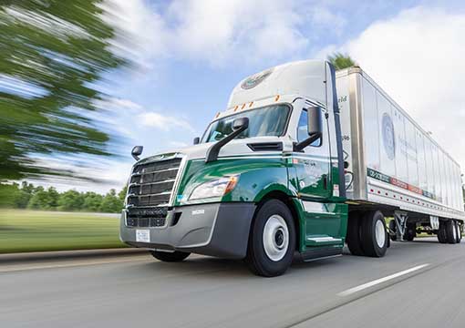 An OD semi-truck drives on a highway, blurred to show motion.