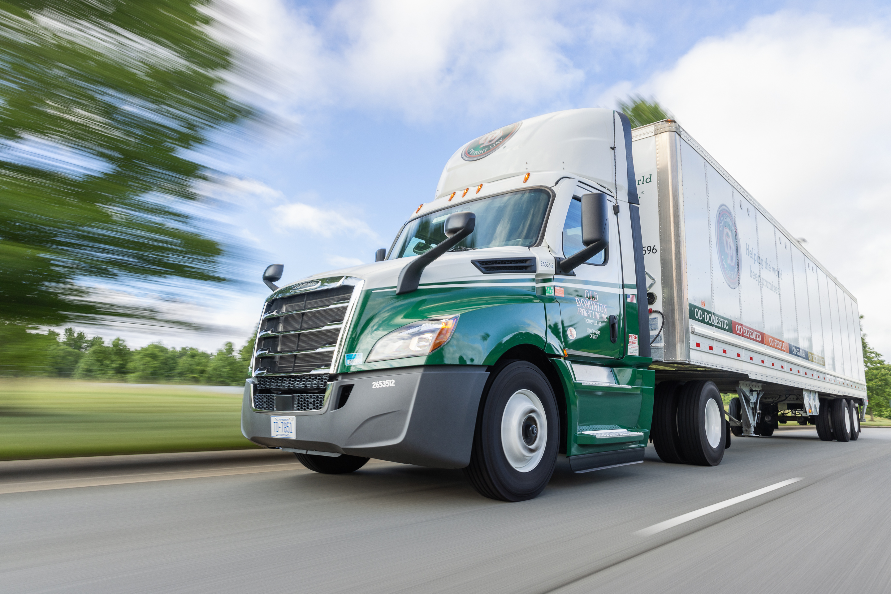 A green and white Old Dominion Freight Line truck speeding down a highway with motion blur in the background.