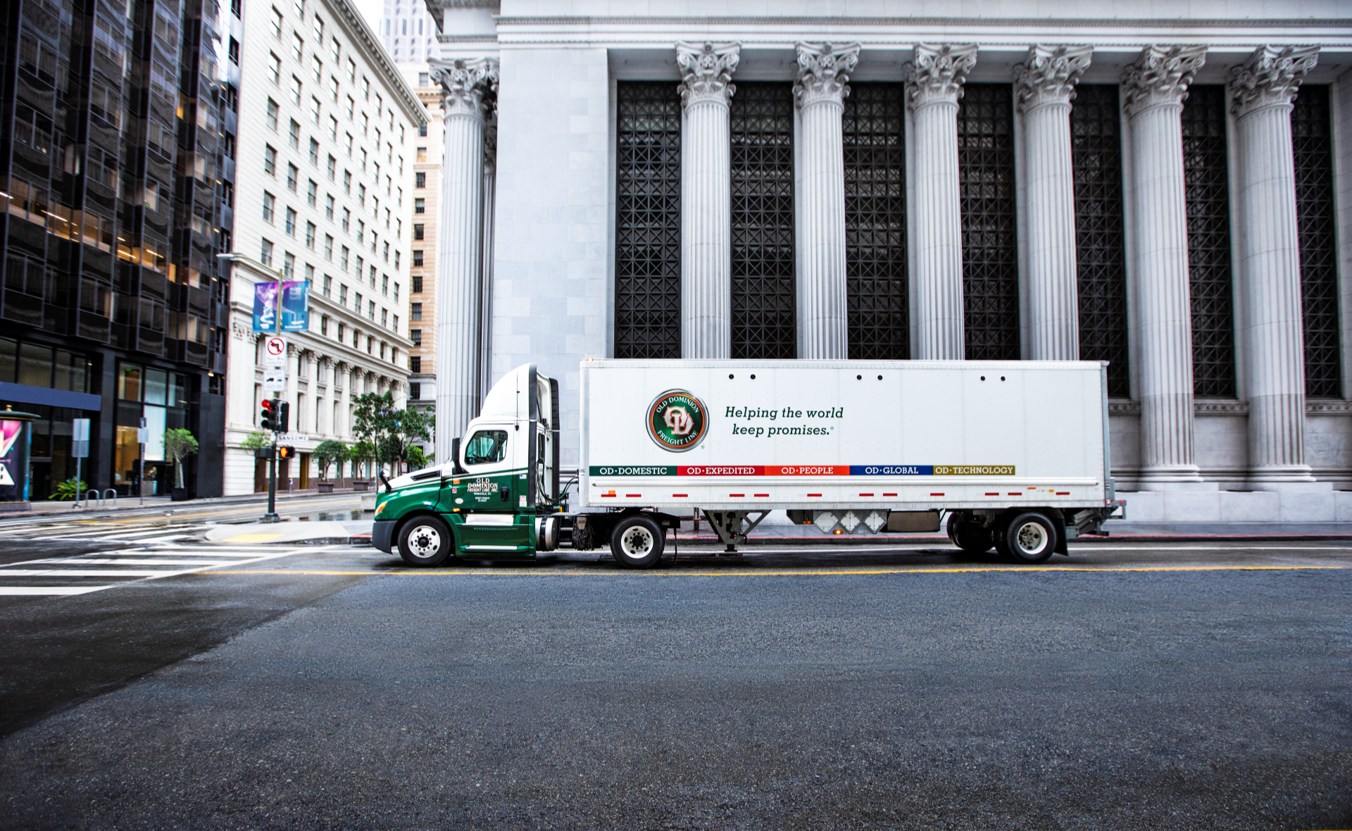 An OD semi-truck drives on a highway, blurred to show motion.