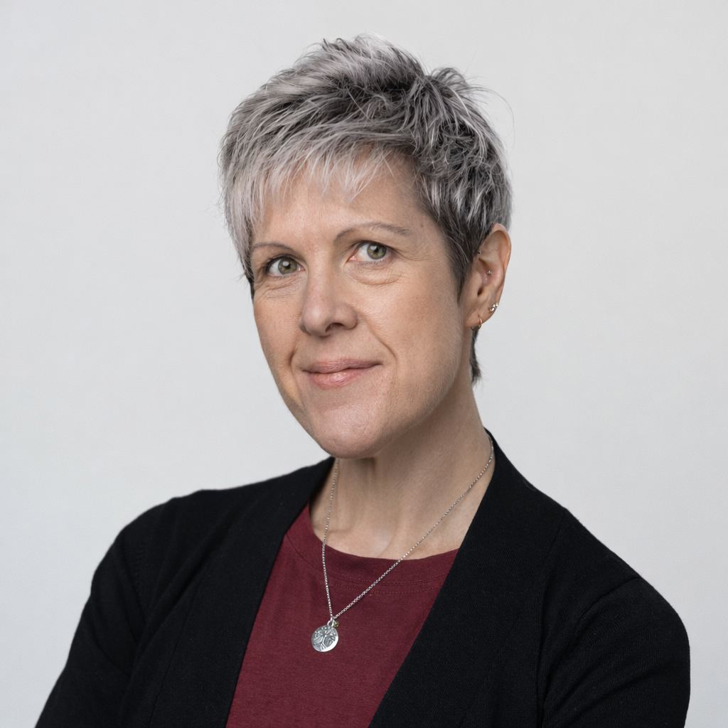 Portrait of a woman with short, spiky grey hair and a friendly expression, wearing a red top and black cardigan.