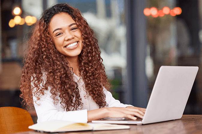 A woman with curly hair smiles as she types on her laptop.