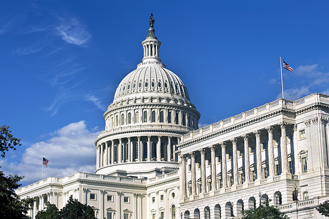 The United States Capitol building stands tall against a bright blue sky.