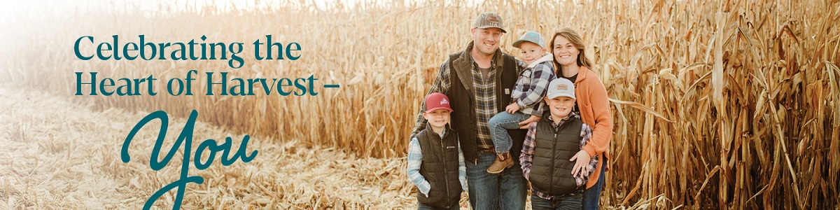 A smiling farm family stands beside a cornfield beneath the message, “Celebrating the Heart of Harvest—You.”