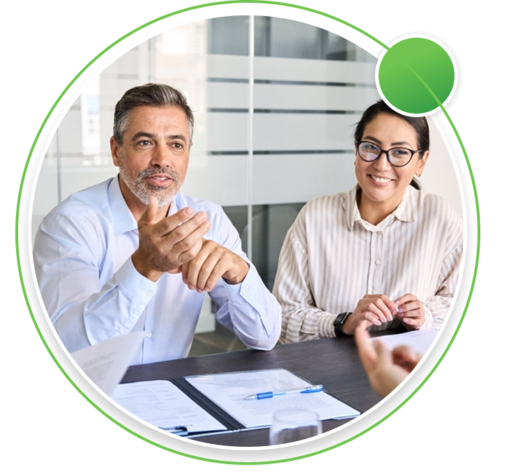 Three professionals in a modern office meeting room, with a man leading a discussion in front of a glass board displaying business charts.
