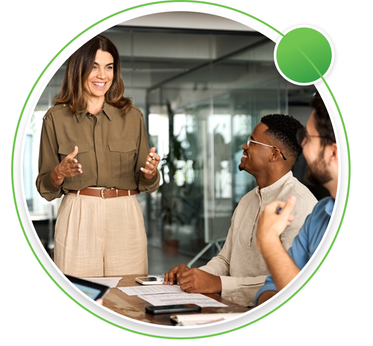 Three professionals in a modern office meeting room, with a man leading a discussion in front of a glass board displaying business charts.