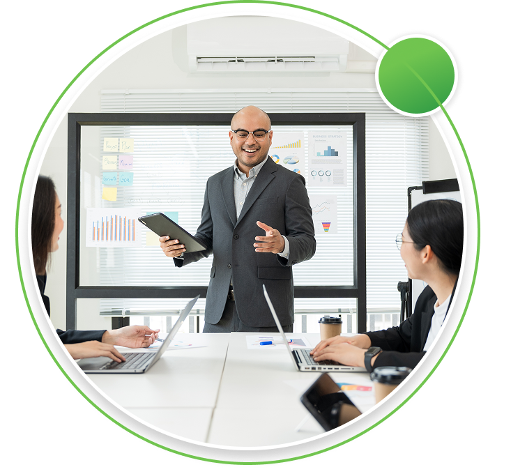 Three professionals in a modern office meeting room, with a man leading a discussion in front of a glass board displaying business charts.
