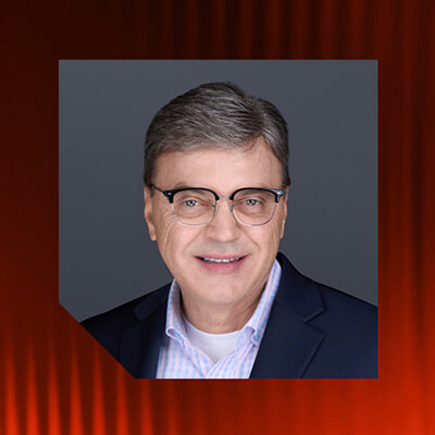 Portrait of a man with short grey hair and black-rimmed glasses, dressed in a blue jacket and light blue shirt.