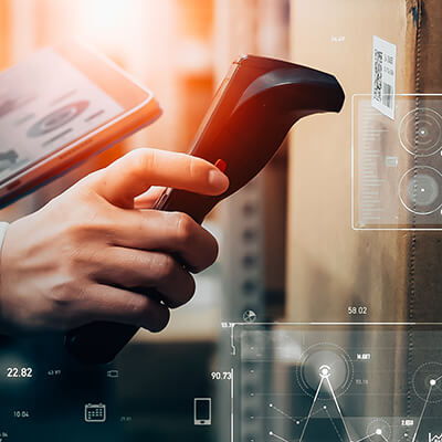 Hand uses a barcode scanner on a package QR code, with digital interface overlays suggesting inventory tracking.