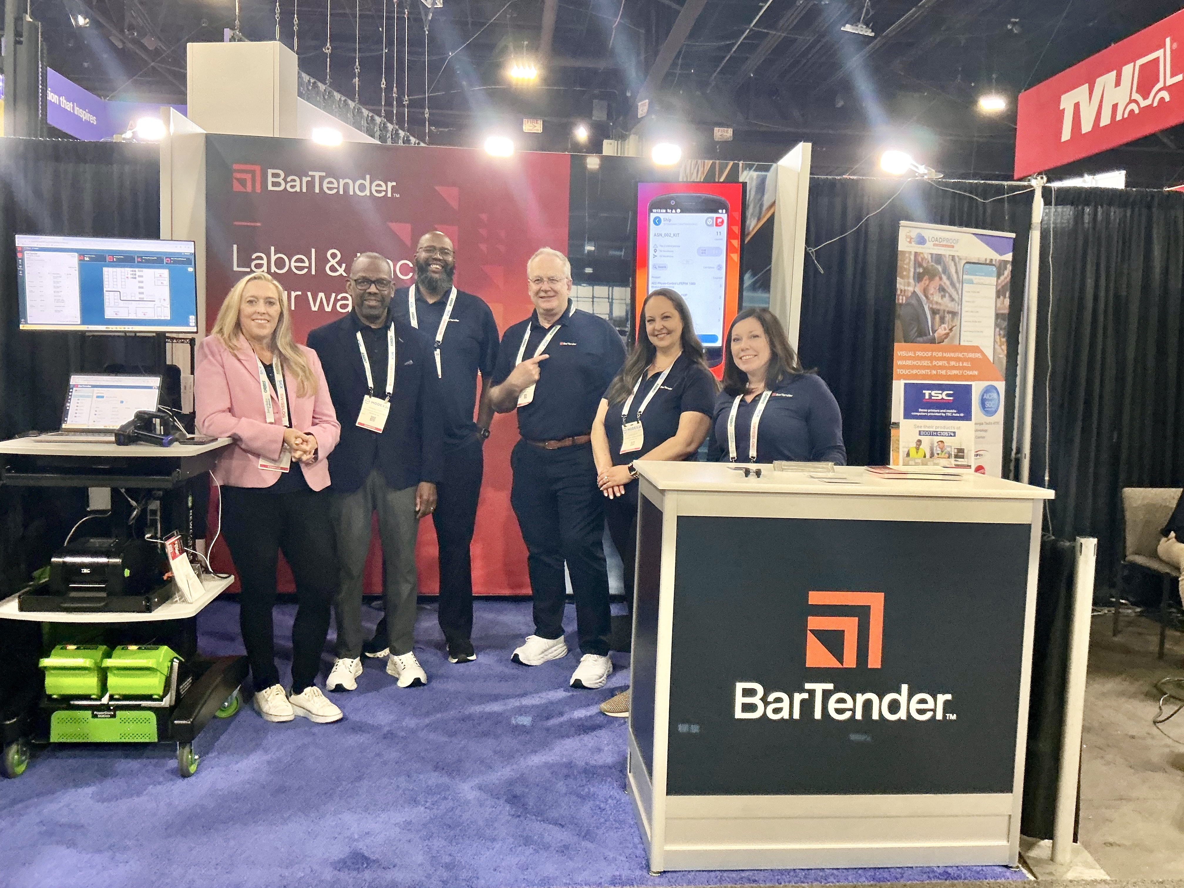 A team of BarTender employees engages with attendees at a trade show booth, showcasing their software