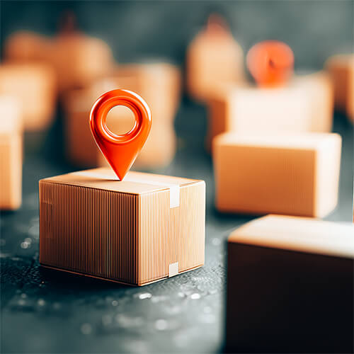 A bright red location pin sits atop a cardboard shipping box, with more blurred boxes in the background.