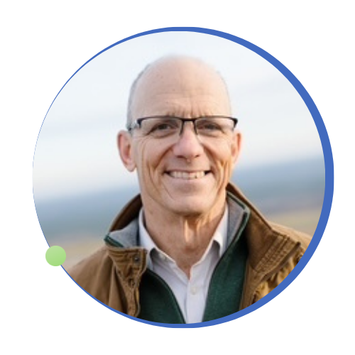 Headshot of a smiling bald man wearing glasses and a brown jacket, framed in a blue circle.